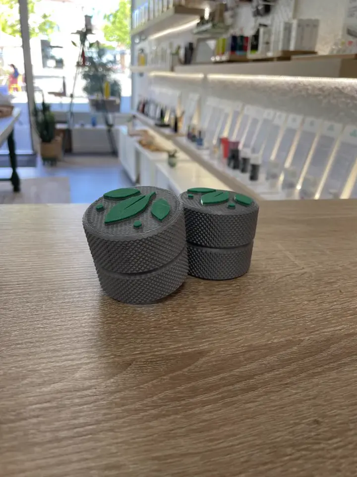 Petites boîtes grises moletées au couvercle à logo vert, posées sur un comptoir