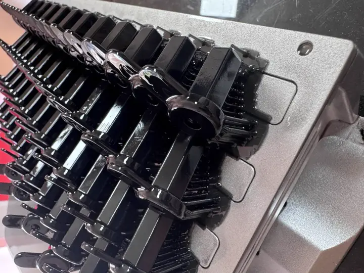 Série de pièces noires identiques imprimées en 3D, alignées sur un support métallique