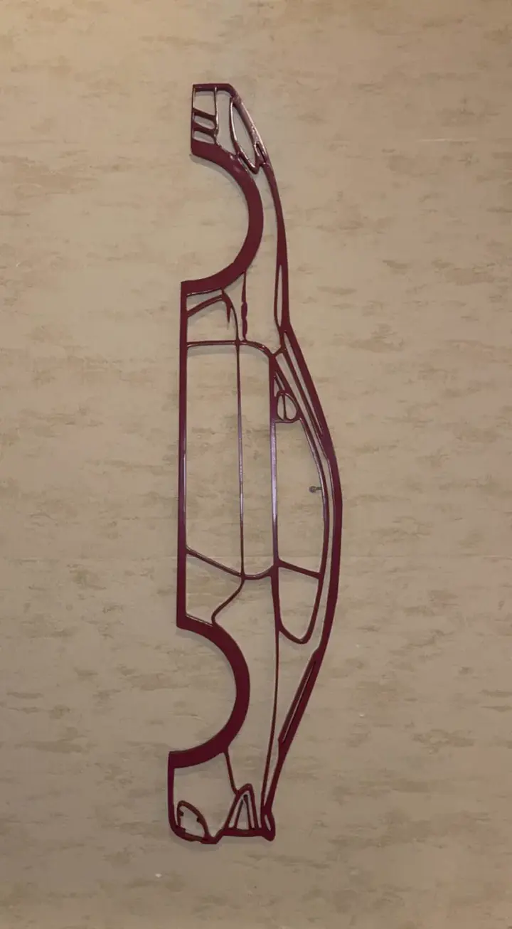 Silhouette filaire d’une voiture de sport imprimée en 3D, fixée sur un mur clair comme décoration