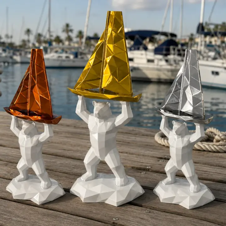 Trois trophées imprimés en 3D : un ours blanc à facettes soulève un voilier bronze, or ou argent